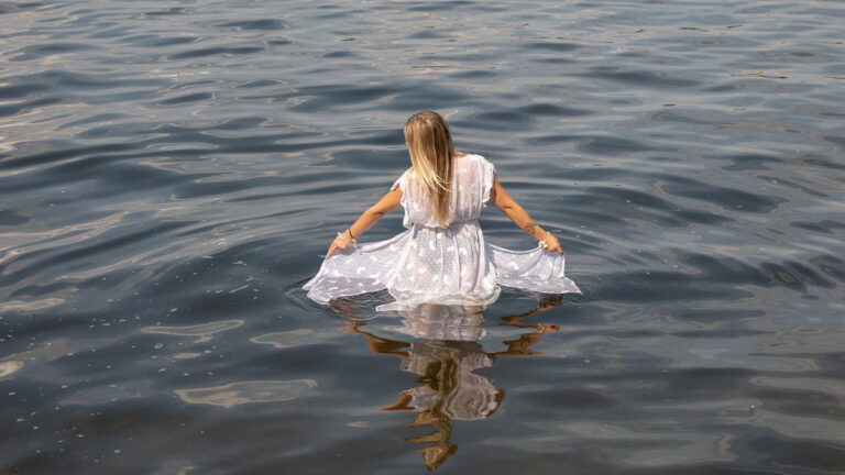 Невеста в белом платье стоит в реке, видно ее отражение в воде